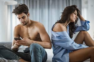 Young woman is feeling depressed while her boyfriend is text messaging on cell phone with some other woman.