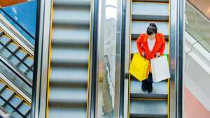 Female shopper standing on escalator with shopping bags in hand.