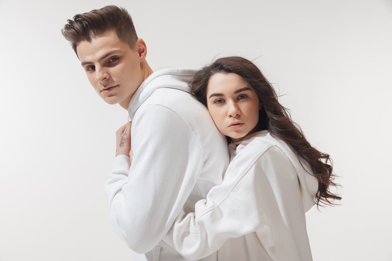 Tender hug. Trendy fashionable couple isolated on white studio background. Caucasian woman and man posing in basic minimal unisex clothes. Concept of relations, fashion, beauty, love. Inclusive.