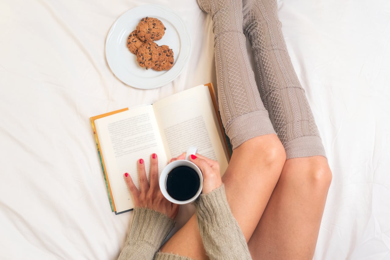 Woman eating breakfast in bed while reading a book .