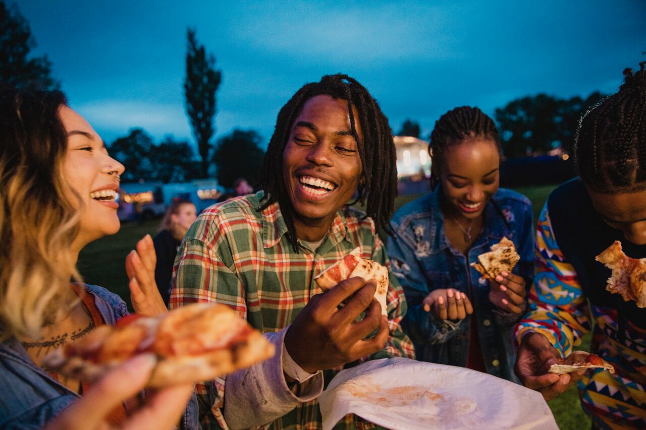 A young group of friends laughing and sharing pizza at a music festival.