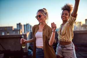 Two women dancing and drinking alcohol at the roof party.