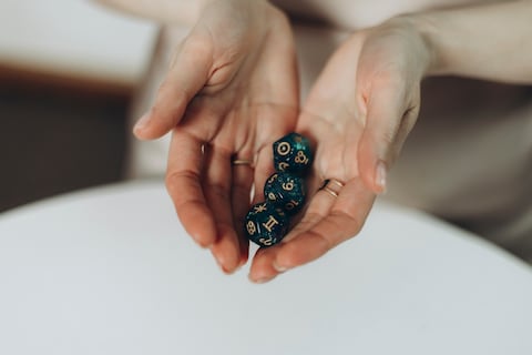A close-up view of female hands holding three emerald 12 sided dice above a white round table.