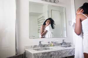 Beautiful black woman drying her face with a towel in the bathroom while looking at herself in the mirror smiling