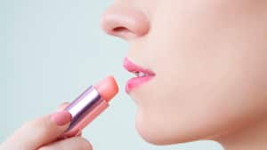 Close-up image of woman applying light peach lip balm to keep lips moisturized
