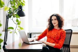 A portrait of a transgender businesswoman sitting at her computer desk and working on a laptop in the office.