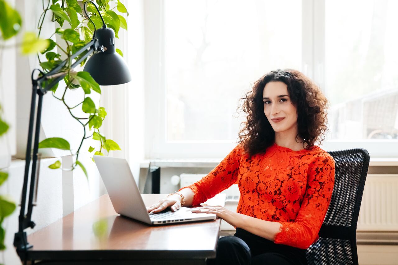 A portrait of a transgender businesswoman sitting at her computer desk and working on a laptop in the office.