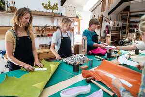 A leather tanner professional teaching her students how to use an awl to mark out the stencil shape for the pair of shoes she is creating out of ethically sourced leather. She is working directly out of an independently owned small business Tannery which is committed to sustainable zero waste working from the studio in Wales. / Female Focus Collection
