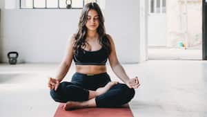 Mujer adulta joven está practicando yoga en un loft moderno. Postura de medio loto o ardha padmasana.