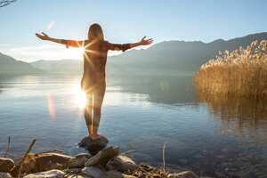 Mujer joven alegre junto al lago disfrutando de la naturaleza. Brazos extendidos por emoción positiva.