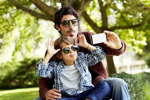 Playful father and son making faces while taking selfie in park