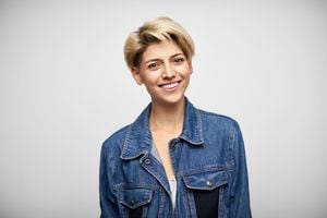 Portrait of smiling young woman in denim jacket. Fashionable Latin American female with blond short hair. She is against white background.